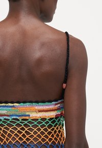 Top all'uncinetto multicolore con design a rete, dotato di una spessa tracolla nera intrecciata e di una banda a strisce colorata lungo il bordo superiore.