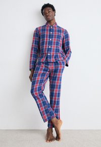 Conjunto de pijama de cuadros en tonos azules y rojos, que incluye una parte de arriba con cuello y botones, y pantalones a juego, fabricado en tejido suave y de corte relajado.