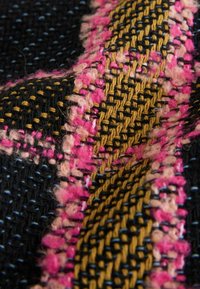 Textilmaterial mit schwarzem Grund und pinken sowie goldenen gewebten Mustern. Die Textur ist flauschig mit deutlich sichtbaren verflochtenen Fäden.