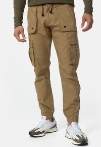Khaki spodnie cargo z dwoma dużymi kieszeniami na klapie, elastycznymi mankietami i sznurkiem w pasie. Wykonane z lekkiego materiału o gładkiej teksturze.