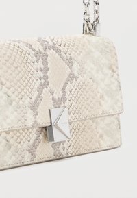 Μικρή ορθογώνια τσάντα χειρός με ανοιχτό μπεζ σχέδιο φολιδωτού δέρματος φιδιού, ασημένιο γεωμετρικό κούμπωμα και ασημένια αλυσίδα λουρί.