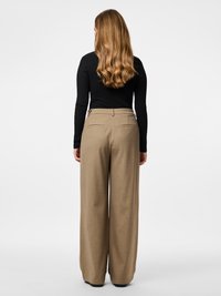 Παντελόνια με ευρύ πόδι σε ανοιχτό καφέ ύφασμα, με απαλή υφή, ραμμένη κοπή και διακριτικές πίσω τσέπες. Φορεμένα με μαύρο μακρυμάνικο τοπ.