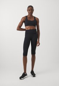 Reggiseno sportivo nero e leggings capri realizzati in tessuto morbido, con una vestibilità aderente e un design minimale, abbinati a scarpe da corsa nere.