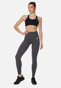 Zwarte sportbh en hooggesneden grijze leggings met een logo. De stof is glad en rekbaar, ontworpen voor sportkleding.