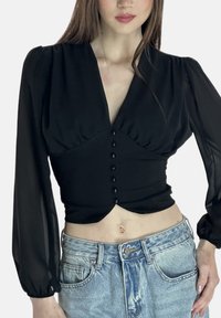 Schwarzes Cropped-Top mit Puffärmeln, geknöpfter Vorderseite und V-Ausschnitt; kombiniert mit hoch taillierten, hellen Jeansshorts. Glatte Textur.