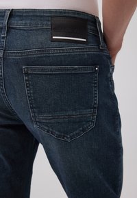 Dunkelblaue Jeans aus Denim mit glatter Textur, ausgestattet mit einem Lederpatch mit der Aufschrift "MAVI ULTRA MOVE" und einer Gesäßtasche mit Steppdetails.