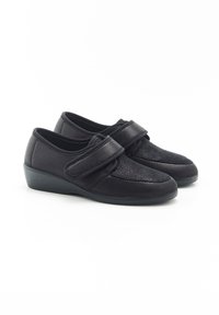 Scarpe nere realizzate in materiali texturizzati con una tracolla in Velcro. Forma arrotondata, tacco basso a cuneo e una combinazione di superfici lisce e decorative.