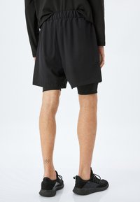 Sorte atletiske shorts med elastisk talje, over knæ længde, og et glat, letvægtigt stof. Kombineret med sorte sneakers.
