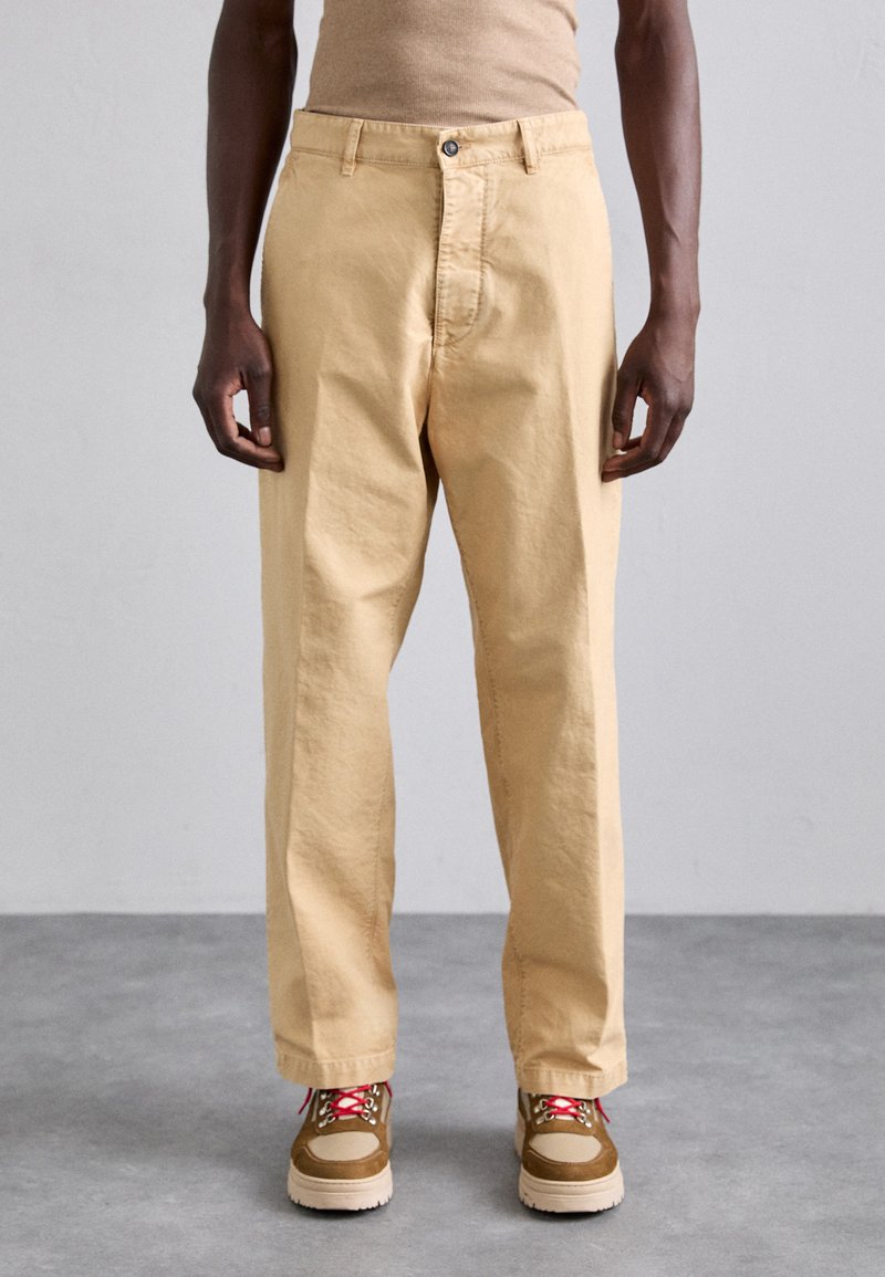 Lys beige bomuldsbukser med en afslappet pasform, der har frontlommer, en knaplukning og bæres med brune og lyserøde sneakers.