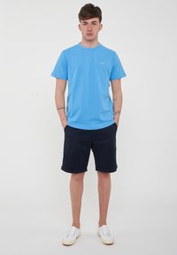 T-shirt azzurro chiaro a maniche corte con collo rotondo, abbinato a pantaloni corti blu scuro. Sneakers bianche completano l'outfit. Design semplice e casual.