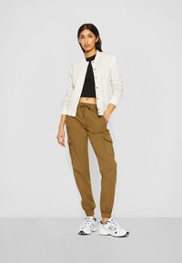 Chaqueta bomber gris claro con botones frontales, top corto negro y pantalones cargo caqui con puños elásticos. Zapatillas blancas con acentos negros.