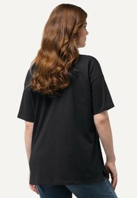 Sort oversized t-shirt med korte ærmer, lavet af blødt stof, med lige snit og sideslidser, båret med mørkeblå jeans.