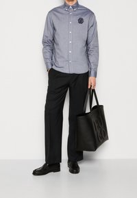 Knappupp skjorta i blå chambray med en logotyp patch, tillsammans med svarta byxor och en stor svart läder tote-väska. Oxford skor fulländar looken.