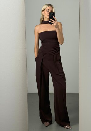 Kvinde med blondt hår iført mørk stropløs top og matchende vidde benbukser, der tager et spejlselfie med en smartphone.