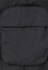 Poche en tissu noir avec un rabat arrondi, bordé de coutures et doté d'une languette horizontale. Texture lisse avec une finition mate.