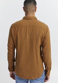 Camisa de cuadros marrón con botones, de manga larga y con dobladillo curvado. Tejido texturizado y cuello estándar. Puños abotonados.