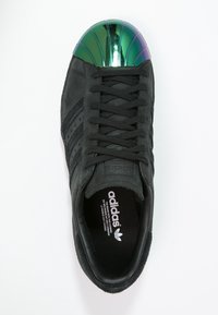 Sneaker in suede nero con tre strisce nere, lacci testurizzati e punta a conchiglia riflettente verde e viola. Presenta un logo Adidas sulla linguetta.
