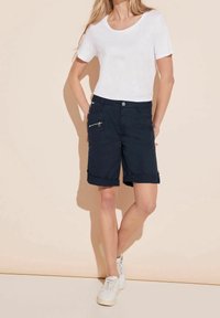 Marinblå shorts med uppvikt fåll, en dragkedjeficka och knäppning. Kombineras med en åtsittande vit t-shirt och vita sneakers.