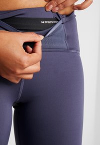 Speed Pocket leggings in dark purple fabric feature a hidden pocket at the waistband and smooth stitching for comfort and functionality.