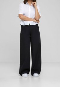 White short-sleeve button-up shirt paired with loose black trousers and white sneakers. The outfit features a relaxed fit and simple design.