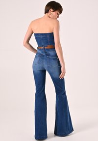 Blauwe denim jumpsuit met een strapless top, wijde broekspijpen en een bruine riem. Beschikt over twee achterzakken en een getailleerd ontwerp.
