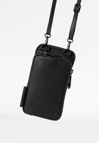 Black crossbody bag made of textured leather with a zip closure, adjustable strap, and a side pocket for small items.