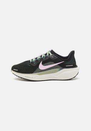 Zwarte Nike hardloopschoen met lichtroze swoosh, lichtgroene accenten, witte gedempte zool en reflecterende details op een witte achtergrond.