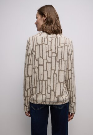 Beżowy sweter z dzianiny z geometrycznym wzorem w ciemniejszym beżu. Miękka faktura, długie rękawy, ściągacz na dole i okrągły dekolt. W zestawieniu z ciemnymi jeansami.