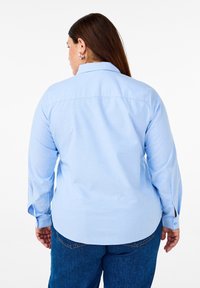 Camicia azzurra chiara con maniche lunghe, vista posteriore mostra il colletto e i polsini con bottone, il tessuto sembra liscio, abbinata a jeans blu scuro.