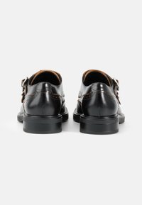 Zwarte leren schoenen met een gladde afwerking, met een ronde vorm, een lage hak en een verstelbare gesp aan de zijkant.