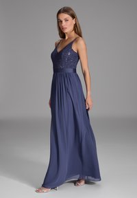 Navy blue iltapuku, jossa on strassikoristeinen bodice, ohut hihna ja virtaava hame satiinivyöllä.