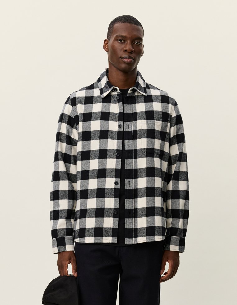 Fekete-fehér kockás ing, flanel anyagból készült; gombos elülső rész, gallér, és egy bal oldali zseb jellemzi.