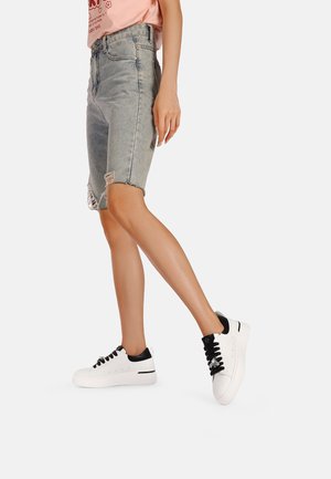 Bermuda shorts in denim bluastro con orlo sfrangiato, abbinati a sneakers bianco e nere con lacci neri e suola texture.