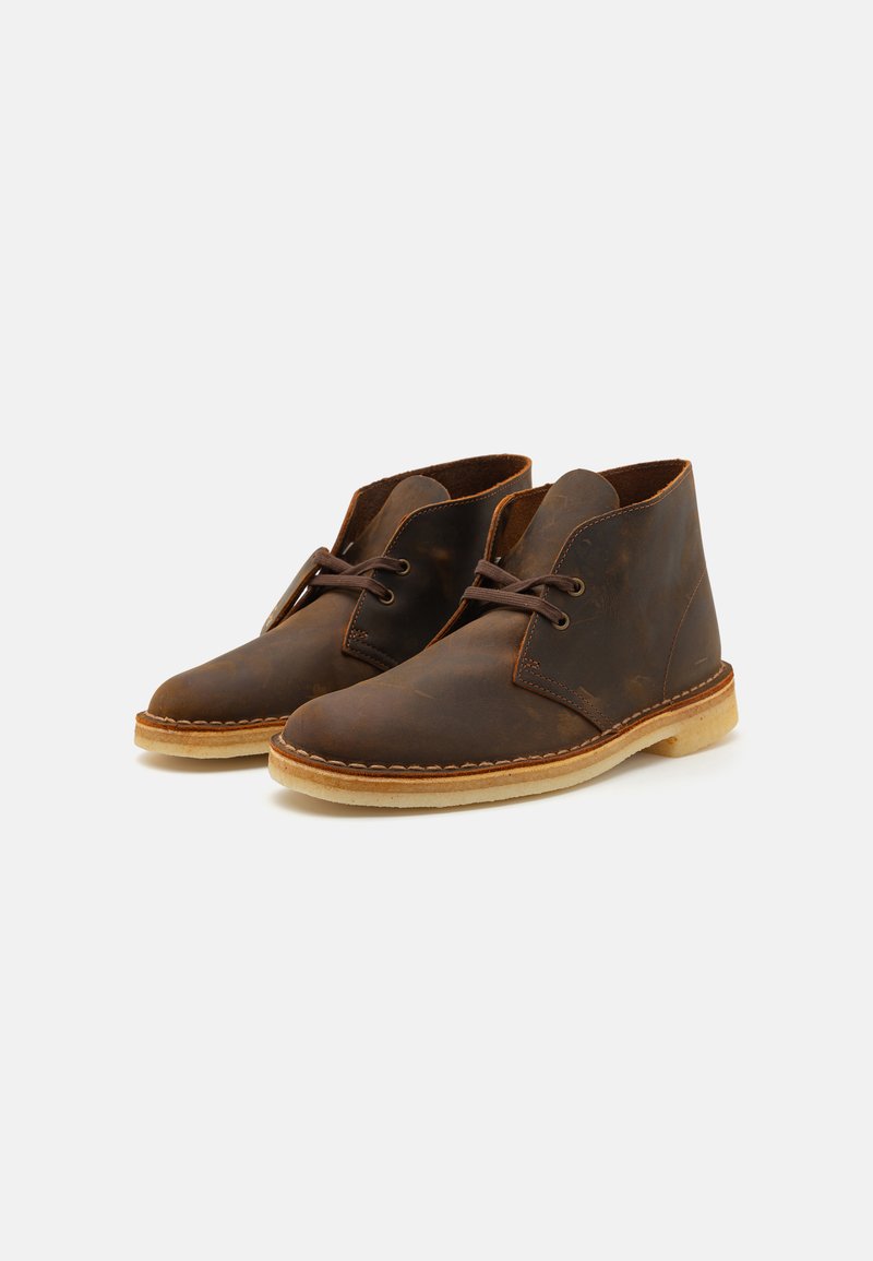 Stivali ankle in pelle marrone con una superficie liscia, punte rotonde e design con lacci. Suole in gomma di colore chiaro a contrasto e dettagli in cucitura.