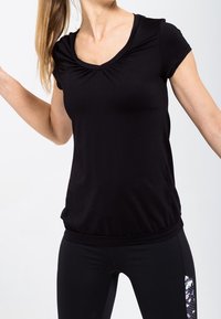 Top negro sintético de manga corta con escote redondeado, detalle fruncido en la parte delantera y silueta ajustada, combinado con leggins deportivos negros.