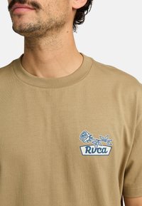 Beige katoenen t-shirt met een grafisch ontwerp van een blauwe roos en logo aan de voorkant. Ronde hals met ribgebreide afwerking, casual pasvorm, gladde stoftextuur.