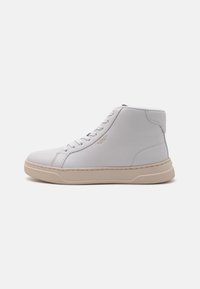 Biele kožené high-top tenisky s textúrovaným povrchom, s béžovými gumovými podrážkami a šnúrkami, a zlatým logom na boku.