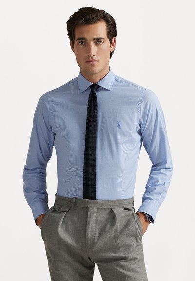 Camicia a righe azzurre con colletto a punta, polsi abbottonati e vestibilità slim, abbinata a pantaloni grigi su misura e una cravatta scura.