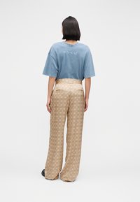 Mėlyni per dideli marškinėliai su siuvinėtais užrašais ant nugaros derinami su smėlio spalvos platėjančiomis kelnėmis su raštais ir aukštu juosmeniu.