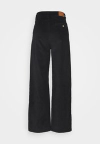 Schwarze Cordstoff-Hose mit weitem Bein und strukturiertem Stoff. Verfügt über eine Gesäßtasche sowie ein braunes Lederpatch am Bund.