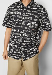 Chemise noires à manches courtes avec texte et logos blancs, comportant divers styles et motifs. Fabriquée en tissu léger, coupe décontractée.