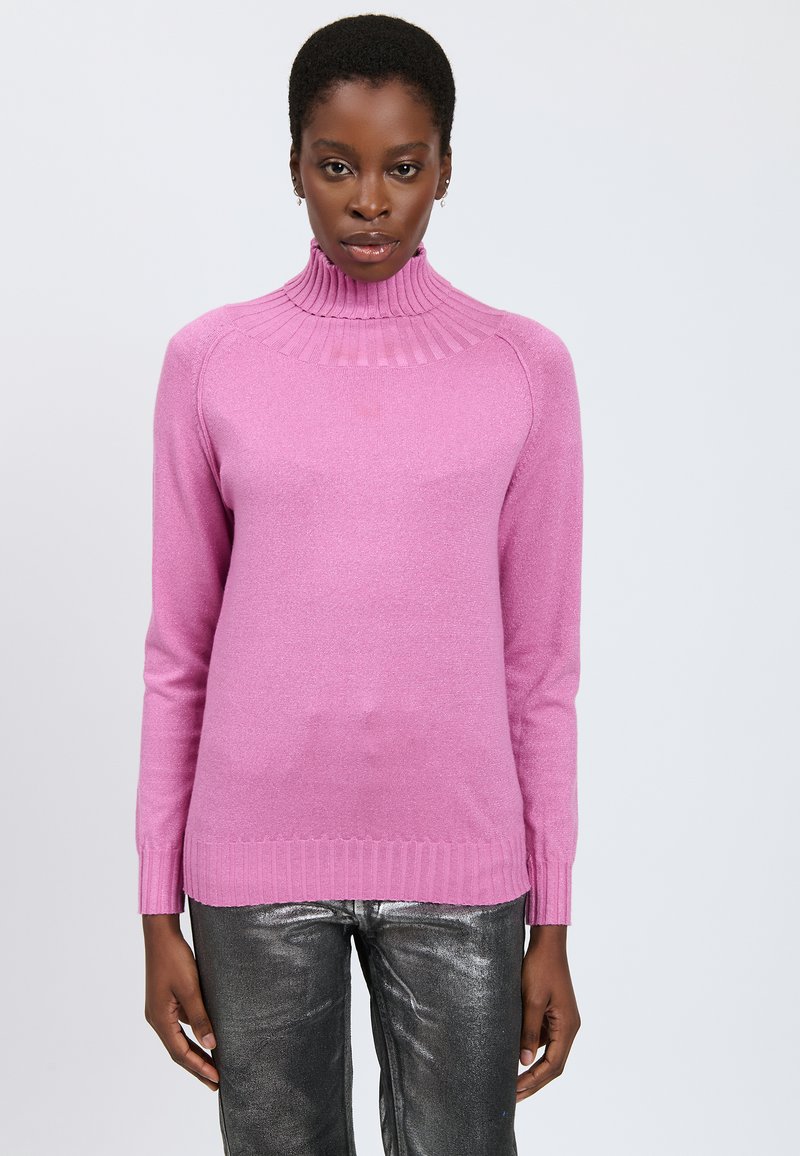 Rippstrick-Turtleneck-Pullover in leuchtendem Pink, aus weichem Strickmaterial, mit langen Ärmeln und lockerer Passform. Kombiniert mit glänzenden silbernen Hosen.