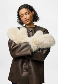 Brązaczkowa skórzana kurtka z dużymi jasnobeżowymi futrzanymi mankietami. Gładka tekstura z pojedynczym zapięciem na guzik i prostym designem.