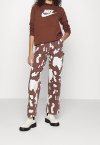 Brown Nike sweatshirt with white logo, paired with brown and white cow-print wide-leg pants and cream-colored ankle boots with black soles.