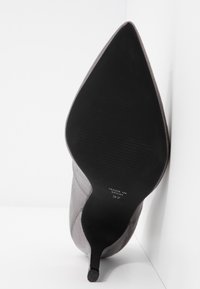 Grå højhælet sko med spids tå, glat tekstur og slank stiletto-hæl. Sort gummisål med ribbet mønster. Str. 37, lavet i Spanien.