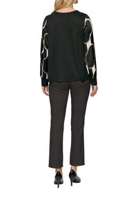 Haut noir à manches longues avec des manches à motif contrasté, associé à un pantalon slim sombre et des chaussures à talons hauts noires.