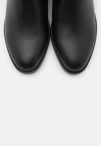 Bottines en cuir noir avec une finition lisse, bout pointu et bordure texturée autour de la semelle, sans quincaillerie ou accents visibles.