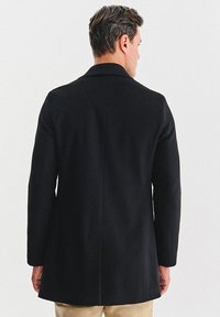 Czarny płaszcz o strukturalnym kroju, z długimi rękawami i pojedynczym rozcięciem z tyłu. Posiada klasyczny kołnierz i gładką fakturę tkaniny.