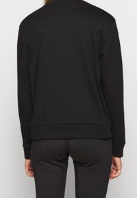Sweatshirt noir au toucher lisse, col rond et poignets côtelés. Conçu avec une coupe décontractée et un style simplifié et minimaliste.