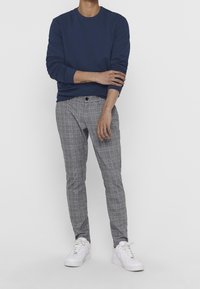 Granatowy sweter typu crewneck, szare spodnie w kratę, białe trampki. Sweter ma ściągacze w rękawach. Spodnie charakteryzują się gładkim przodem i dopasowanym krojem.